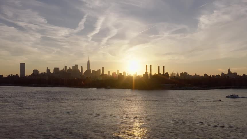 A stunning sunset silhouettes the iconic Manhattan skyline over the East River as a small boat cruises by