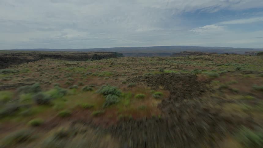 An expansive aerial shot pulls back from a still green lake nestled within a vast rocky coulee, revealing an endless arid landscape