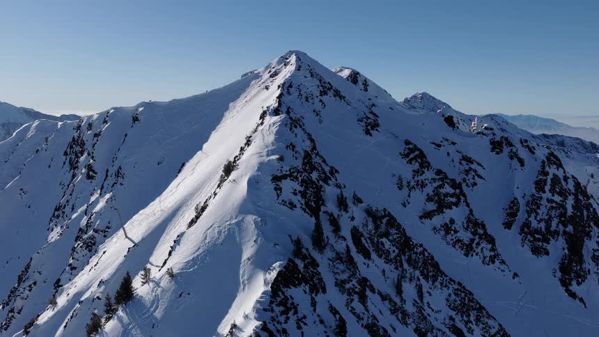 A slow aerial reveal of a majestic, snow-covered mountain range on a bright, clear winter day