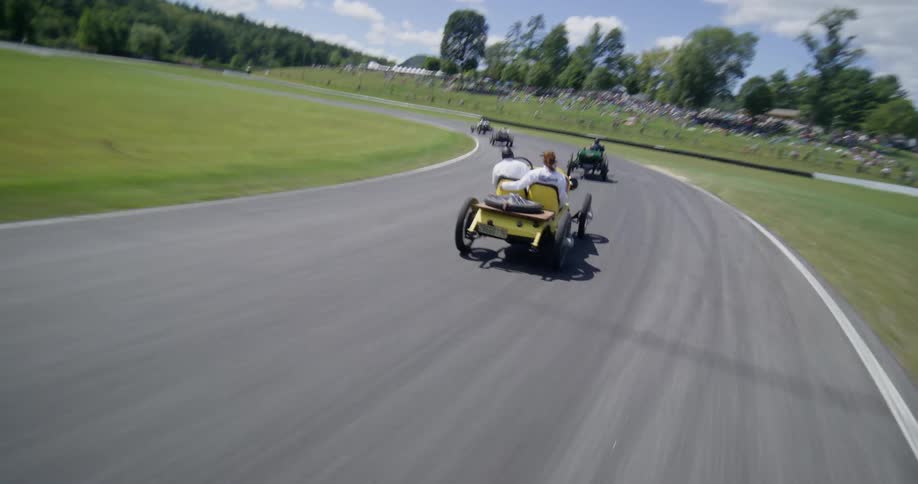Point-of-view from a vintage race car speeding around a track during a classic motorsport event, followed by a dynamic aerial shot