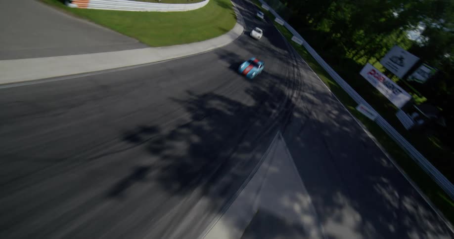 An FPV drone captures thrilling aerial views of vintage cars racing on a scenic track before revealing the lush, green mountain landscape