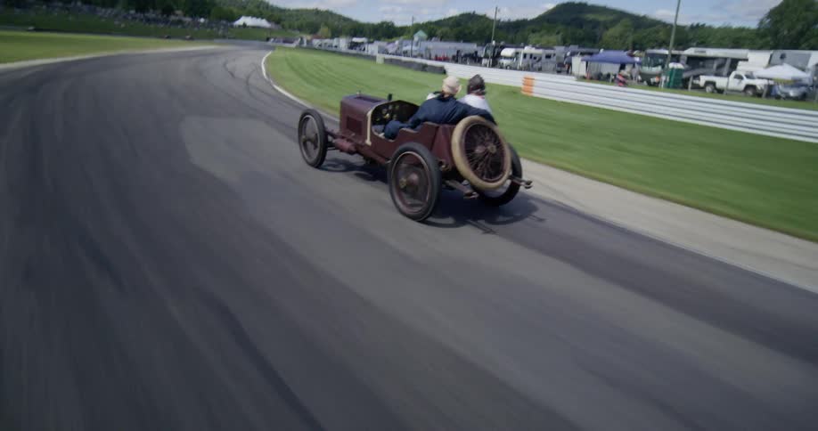 Two men take a thrilling ride in an antique open-wheel race car as it speeds around a winding track in the countryside