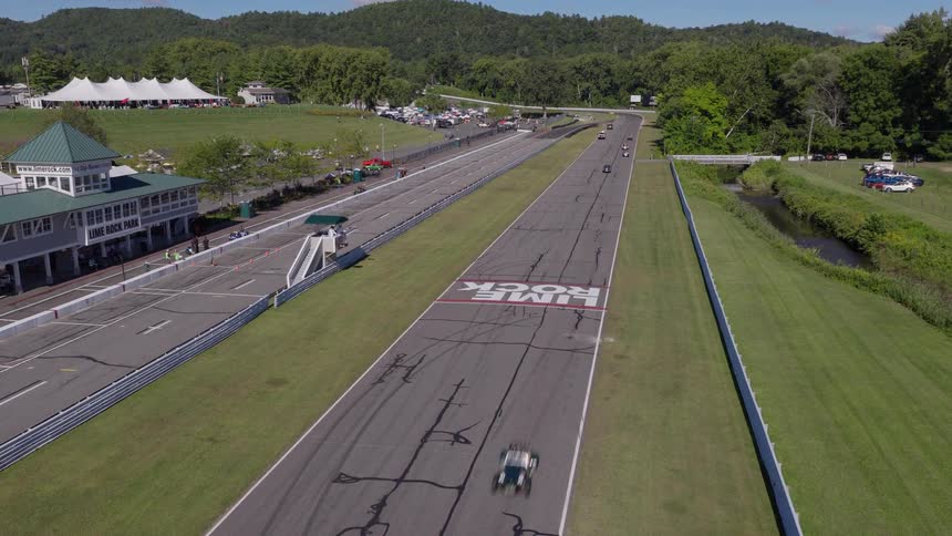 Aerial view of various vintage race cars speeding down the straightaway at Lime Rock Park on a sunny day