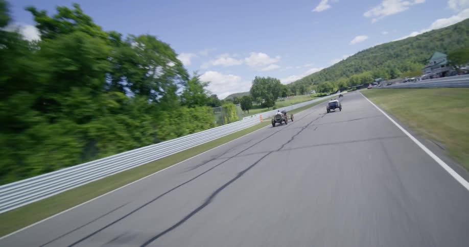 Dynamic aerial and point-of-view shots follow vintage open-wheel race cars as they speed around the scenic Lime Rock Park race track