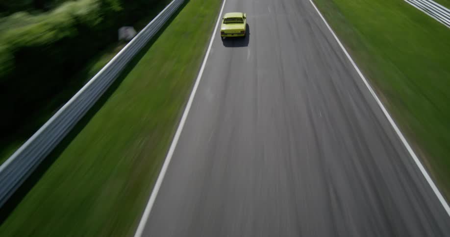 Dynamic aerial footage follows classic race cars as they speed along a winding racetrack surrounded by lush green scenery