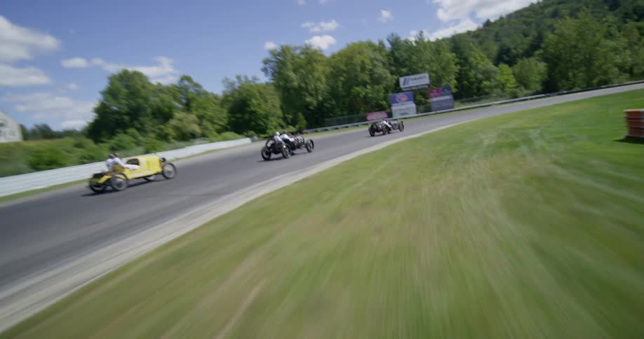 An exciting aerial view follows a group of colorful vintage race cars as they compete on the Lime Rock Park track on a beautiful sunny day