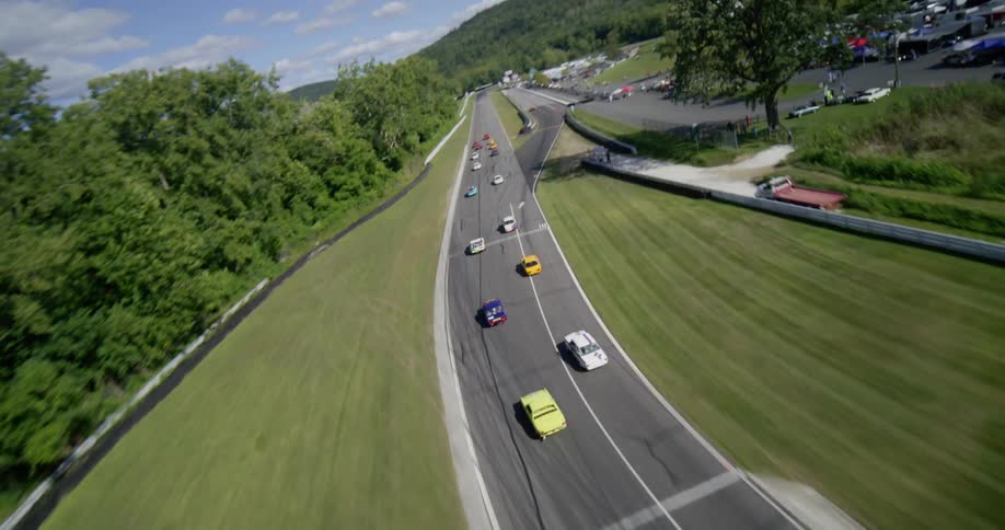 A thrilling aerial shot follows a vintage car race as it speeds around a beautiful, winding track surrounded by lush green hills