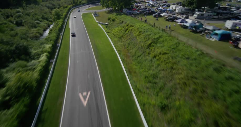 Dynamic aerial shot follows classic race cars speeding around a winding track through a lush, green, and hilly landscape