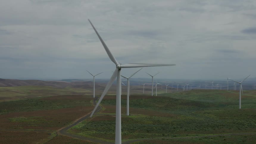 An aerial shot pans from a single spinning wind turbine to reveal an expansive wind farm generating clean energy across rolling hills