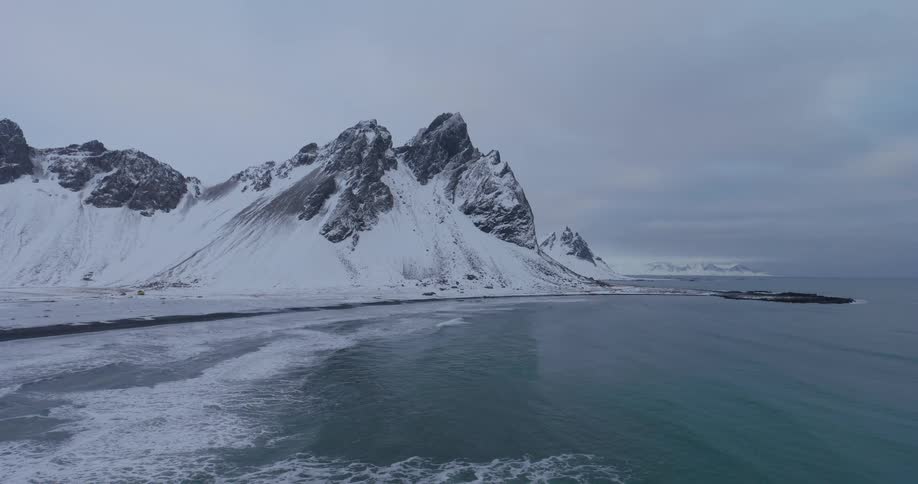 A static shot captures the serene beauty of Iceland's snow-covered mountains meeting the turquoise ocean