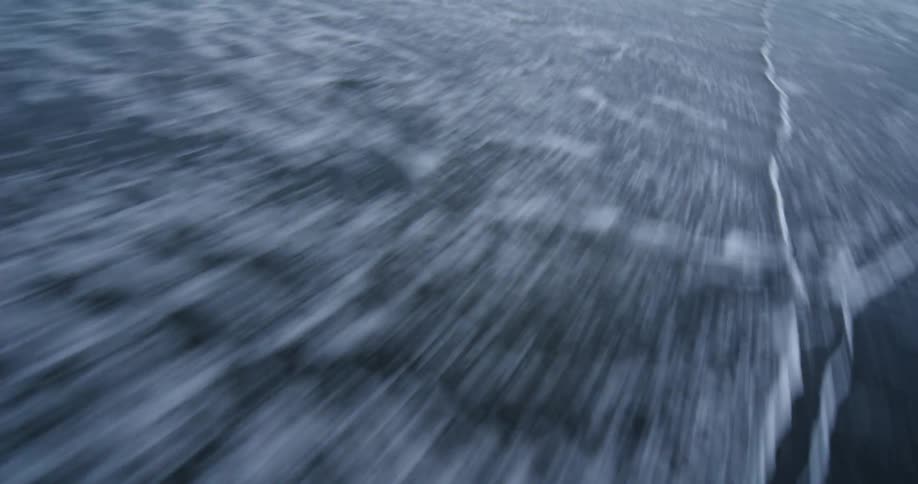 A high-speed, motion-blurred perspective flies low over the ocean surf washing onto a dark sand beach