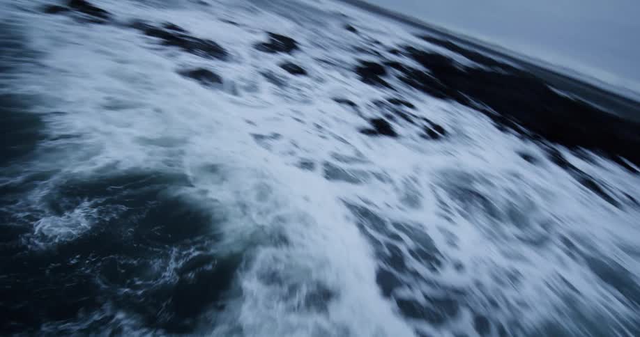 A tilted, low-angle view captures the powerful, churning waves of an icy sea next to a snow-covered coast