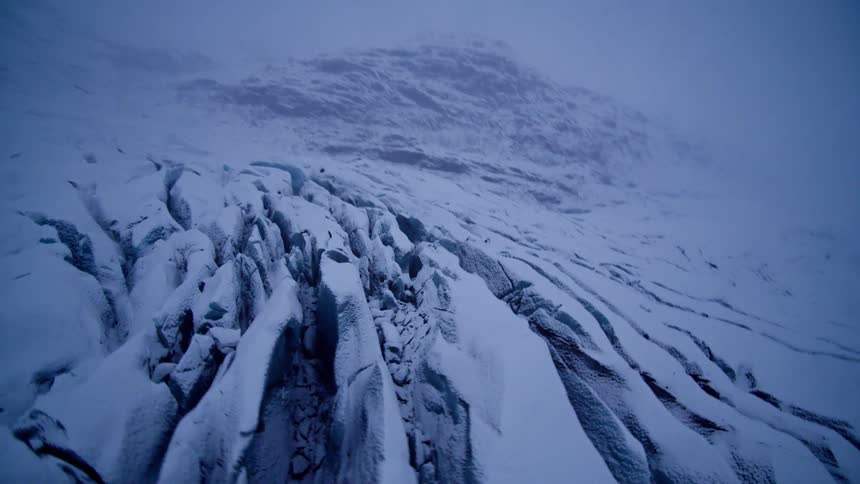 An aerial view reveals the immense and desolate beauty of a snow-covered glacier on a moody, foggy day