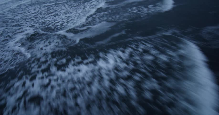 A disorienting high-speed aerial shot flies low over dark, churning ocean waves at dusk