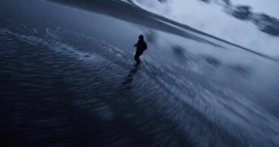 A lone silhouetted figure runs along a dark, wet beach in a moody, canted-angle tracking shot