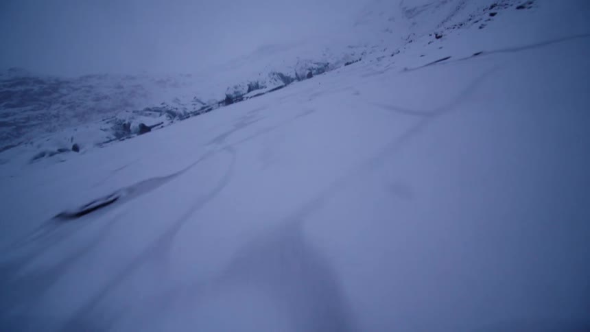 An FPV aerial shot glides low over a vast, snow-covered frozen lake towards a distant glacier in the dim winter twilight
