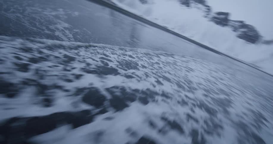 A fast-moving, low-angle shot follows the ocean's tide receding from a black sand beach with snowy mountains in the background