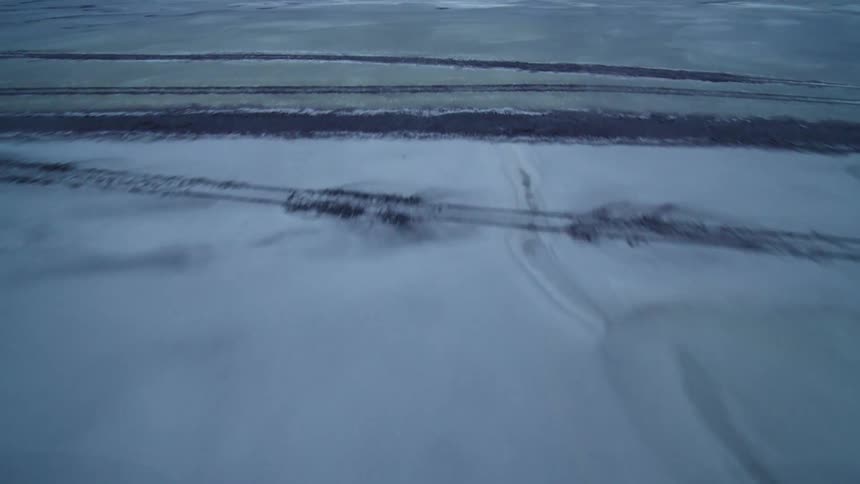 A swift aerial flyover captures the stark beauty of a desolate, frozen, and snow-covered terrain