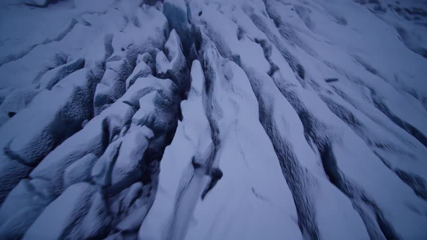An epic aerial journey over the rugged, icy terrain of a vast glacier on a moody, overcast winter day