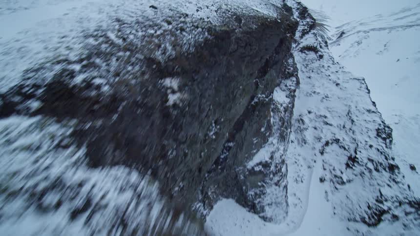 An exhilarating FPV drone shot soars over a rugged and snowy mountain landscape