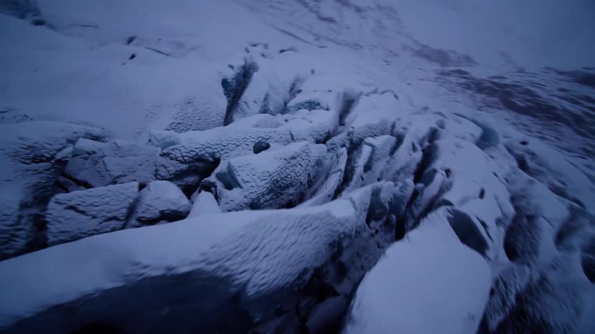 Dramatic aerial shot flying over a vast, snow-covered glacier with deep crevasses on a dark, moody day
