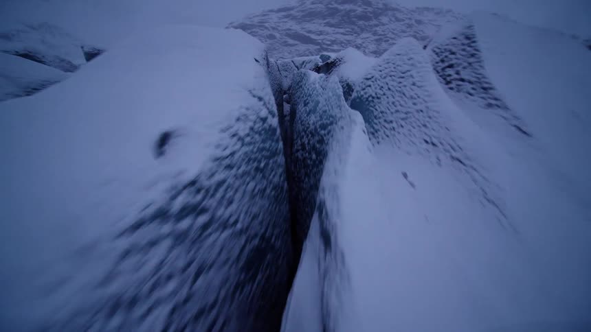 A dramatic FPV drone speeds low over the snow-covered crevasses of a massive, frozen glacier on a dark winter day