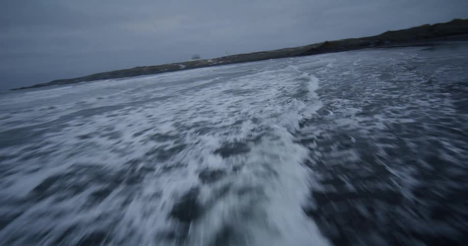 An immersive slow-motion flight over powerful ocean waves crashing onto a desolate black sand beach backed by snow-covered mountains