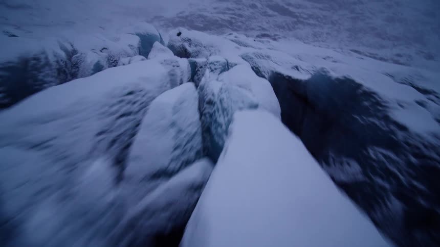 A thrilling, fast-paced aerial flight over the deep crevasses of a vast, snow-covered glacier