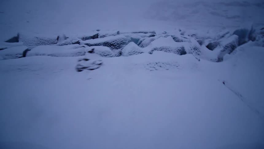 An immersive FPV drone flight speeds over the dramatic, snow-covered terrain of a vast glacier during a foggy winter day