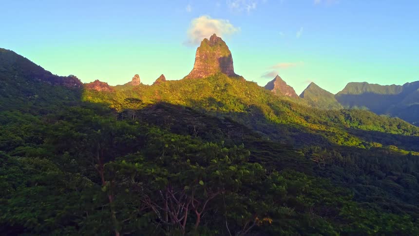 A majestic mountain peak with a single cloud on top towers over a lush green tropical forest during sunrise