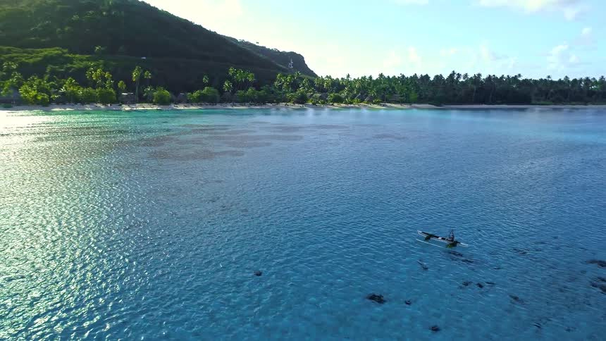 A stunning aerial view captures a person paddling a traditional canoe in the crystal-clear turquoise waters of a tropical island lagoon