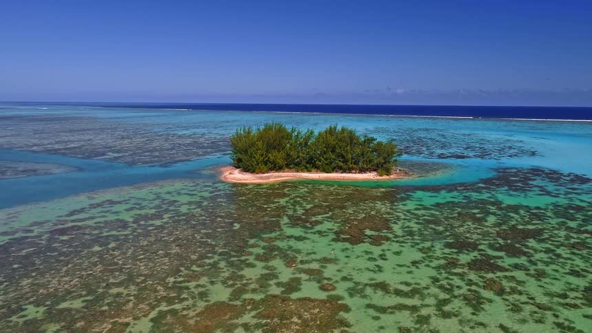 Cinematic aerial pullback reveals a vast coral reef surrounding a tiny, isolated tropical island where a single person floats in the tranquil turquoise water