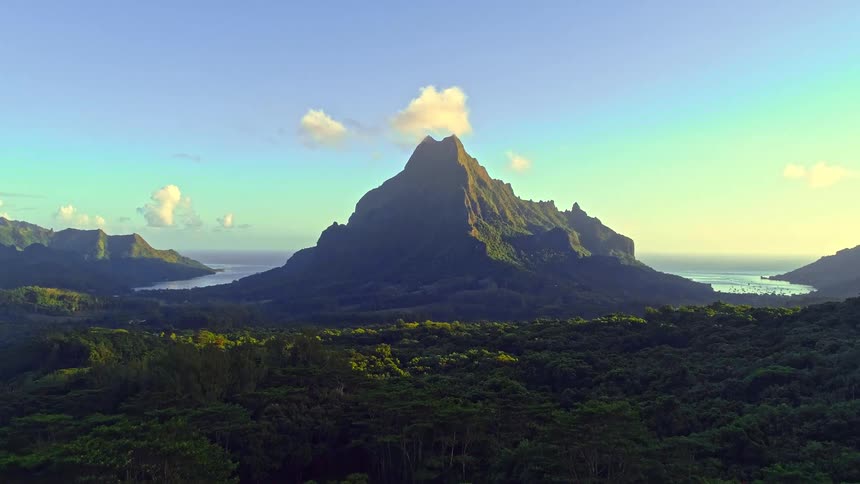 Golden hour light illuminates a magnificent mountain peak towering over a lush tropical jungle and serene ocean bays