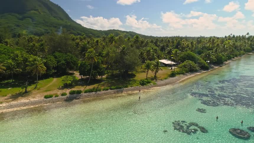 Stunning aerial shot slowly descending over a paradise island with a turquoise lagoon, coral reefs, and palm-fringed shores