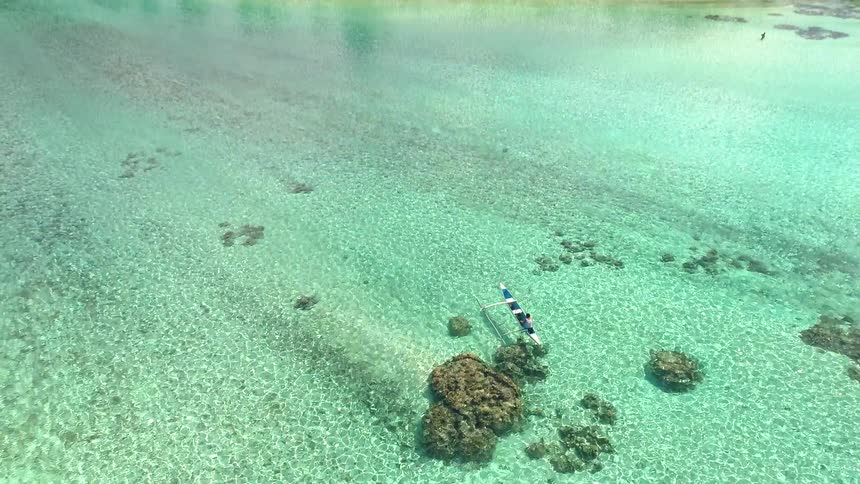 A stunning aerial view pans up from a person in a canoe in clear turquoise water to reveal a lush tropical island and mountain