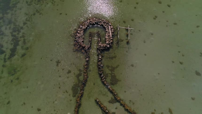 Aerial top-down shot zooms out from ancient stone fish traps in a serene tropical bay