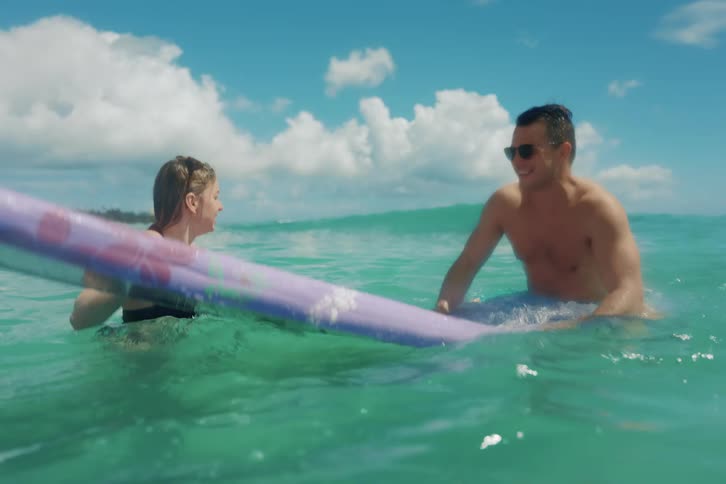 A young couple enjoys a surfing lesson in the beautiful turquoise waters of Waikiki beach on a sunny day