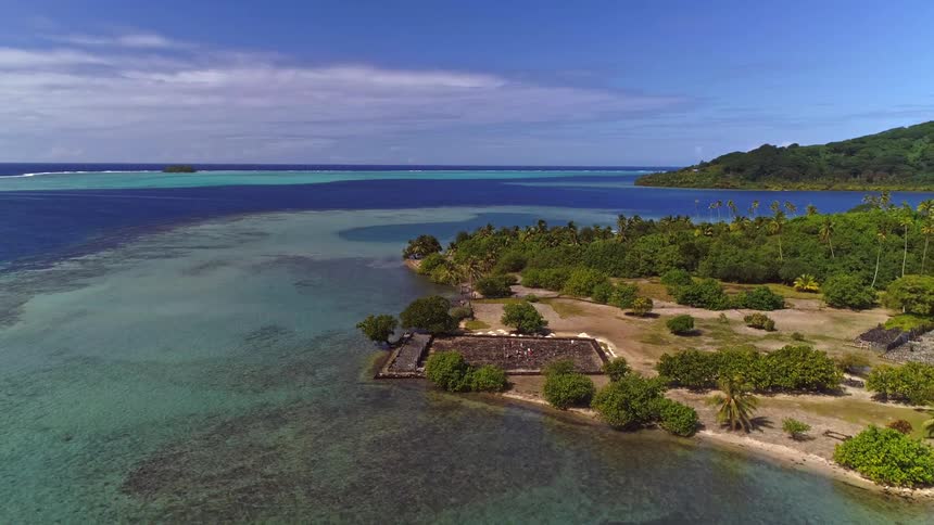 Sweeping aerial view of the ancient Marae Taputapuatea on a lush tropical island coastline surrounded by a turquoise lagoon