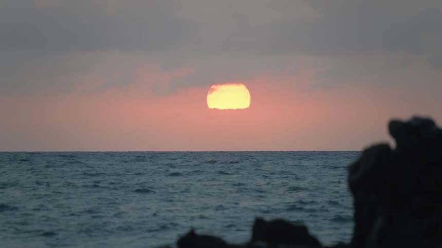 A beautiful sunrise reveals itself from behind the clouds as it reflects on the gentle ocean waves