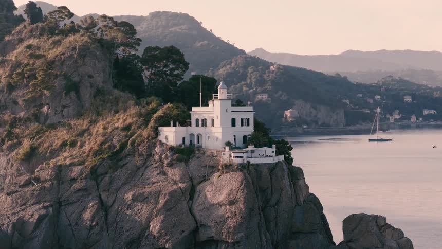 The iconic white lighthouse of Portofino stands majestically on a rugged cliff overlooking the tranquil Ligurian Sea at sunrise