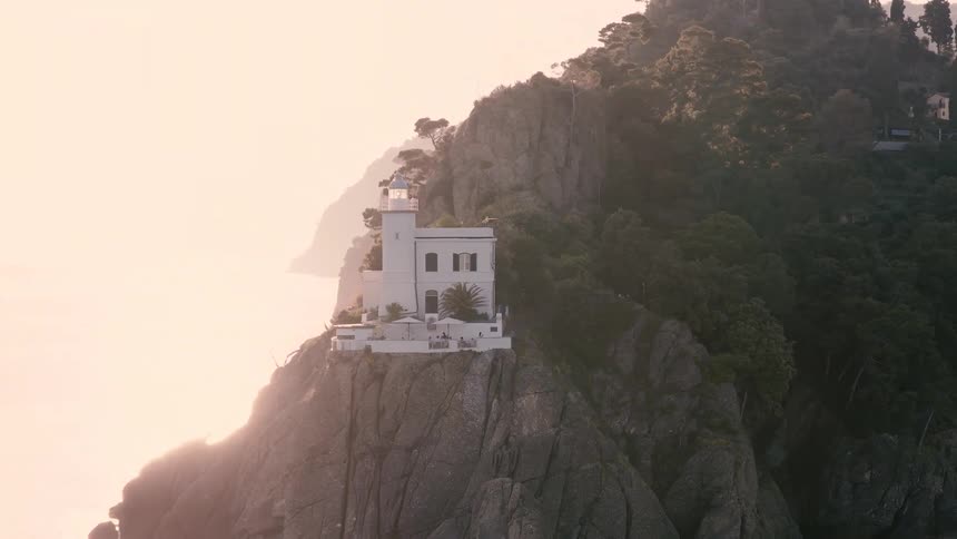 The iconic Portofino Lighthouse stands majestically on a rugged cliff overlooking the tranquil sea at golden hour