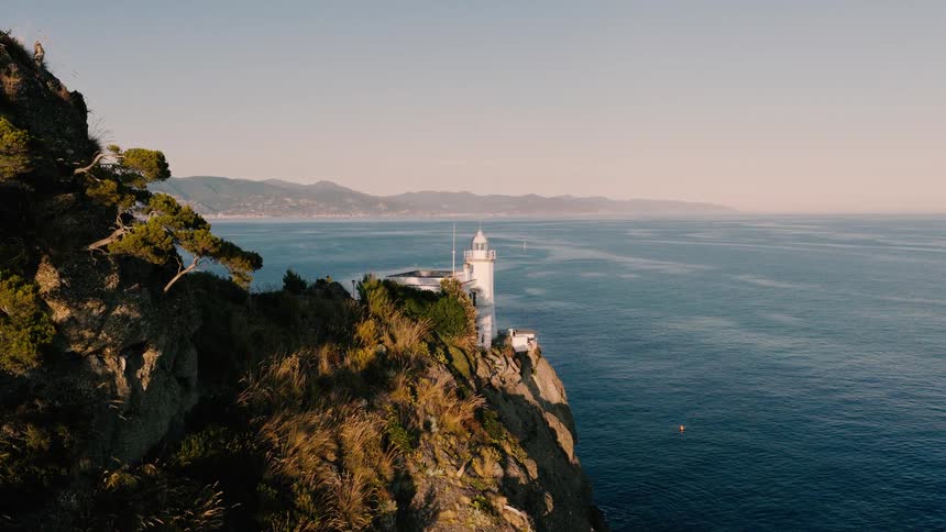 A stunning aerial view of a lighthouse standing on a dramatic cliffside overlooking the vast ocean at golden hour