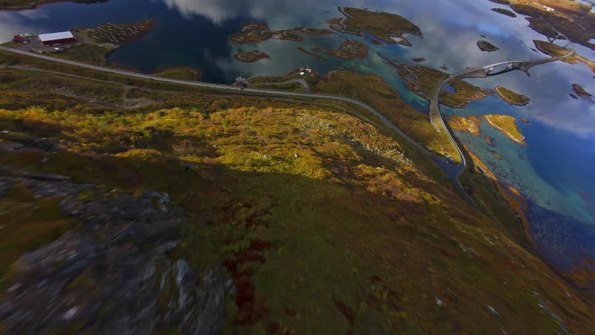 An exhilarating FPV drone dive down a rugged mountain reveals a stunning Norwegian fjord landscape with interconnected islands and calm, reflective waters