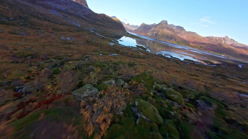 A thrilling first-person-view drone flight descends a colorful autumn mountainside, following a stream down a vast valley towards a tranquil fjord