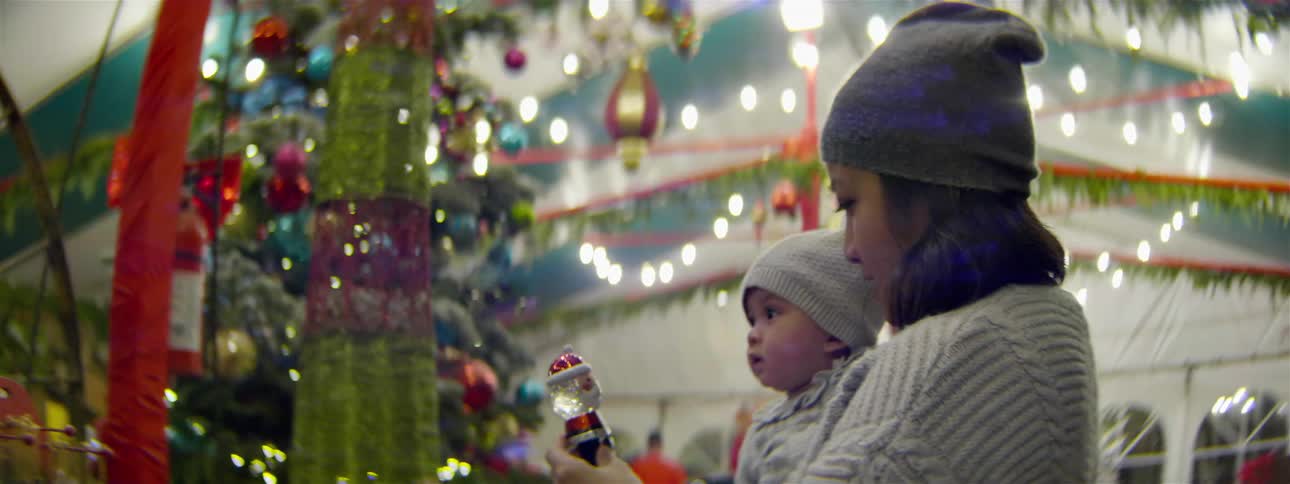 A woman holds a baby while looking at christmas decorations