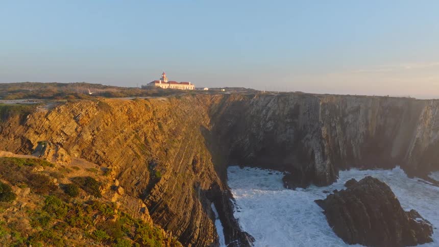 A slow aerial reveal of the stunning Cabo Sardao lighthouse and rugged coastline in Portugal during a beautiful golden hour