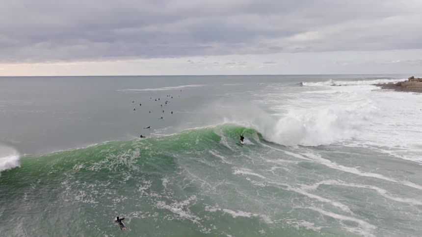 An incredible slow-motion aerial shot captures a surfer riding a massive green wave before a spectacular wipeout