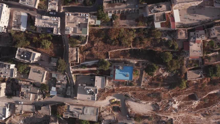 An aerial top-down view slowly rises over a crowded Middle Eastern neighborhood, featuring a bright blue swimming pool