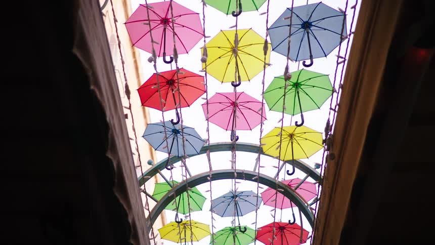 A low-angle view slowly pulls back from a vibrant canopy of multicolored umbrellas hanging as a festive street decoration