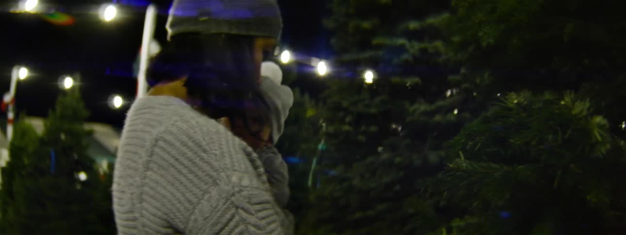 A woman holds a baby while standing in a christmas tree lot